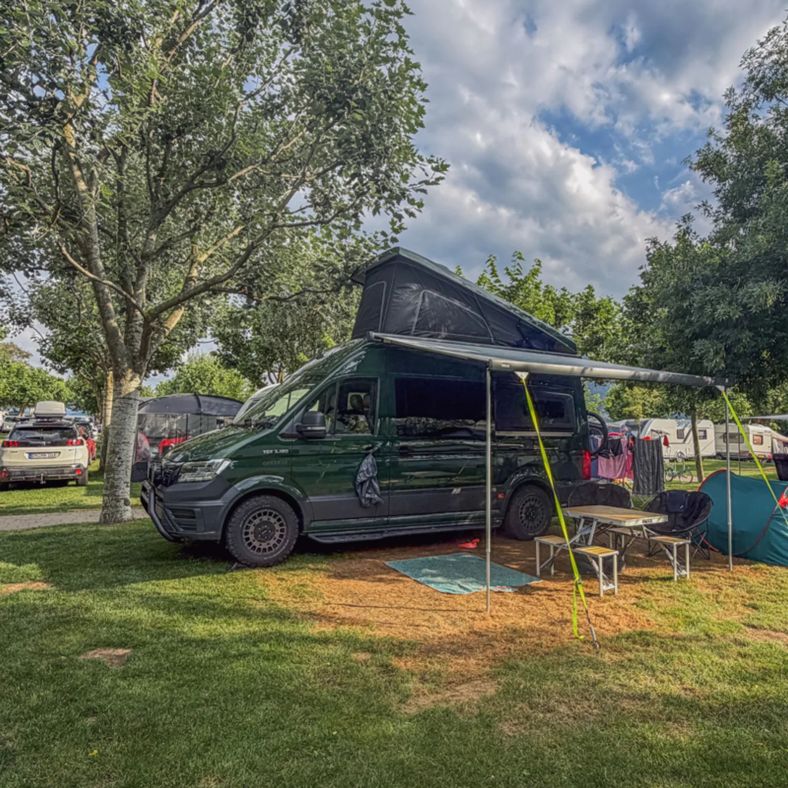 Campervan with pop-top roof up, pitched under a tree at Camping Village Isolino