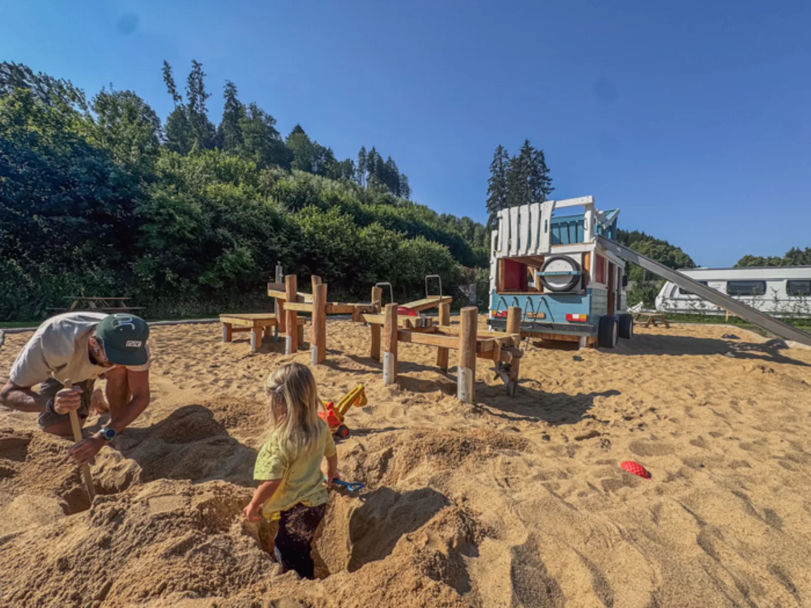 Children digging in the deep sand next to the play area at Camping Wildbach