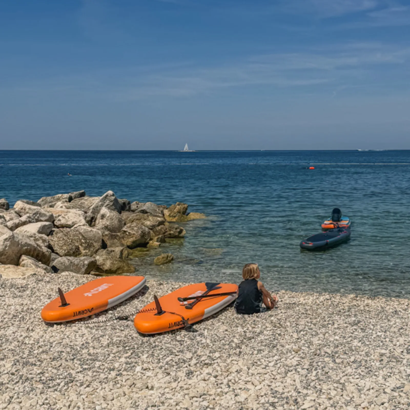 Paddleboards lined up on the pebble beach beside the Adriatic